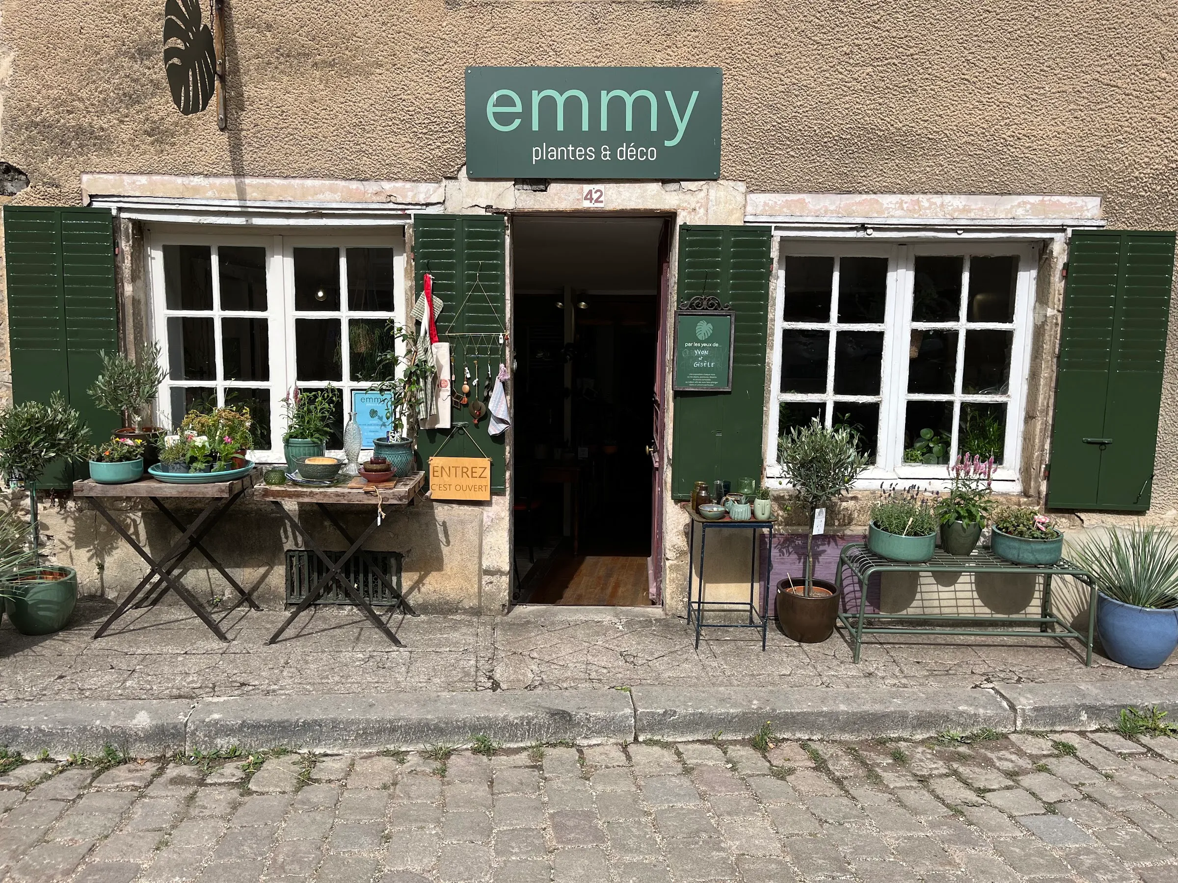 La devanture d'Emmy plantes & déco — volets verts, plantes et poteries sur la rue pavée, Noyers-sur-Serein
